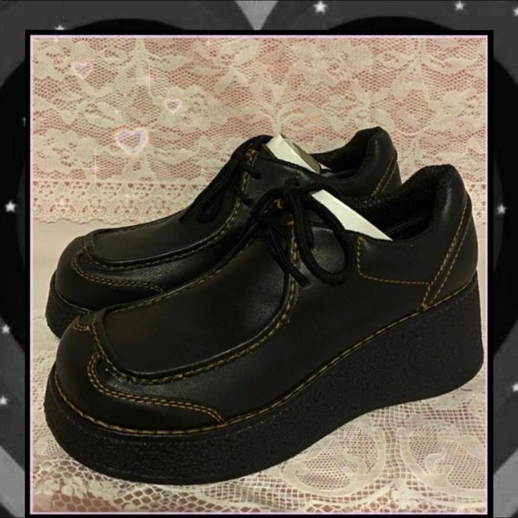 Black chunky-soled 90s platform shoes with three-eyelet lacing and a thick treaded sole, photographed on a patterned surface
